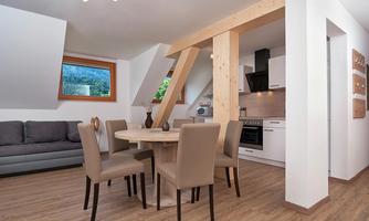 A modern apartment with a cozy living area and an open kitchen. The table is surrounded by chairs and large windows let in plenty of light.