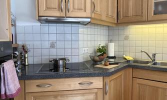 A modern kitchen with wooden cabinets and an elegant countertop. On the stove, there is a pot and fresh ingredients.