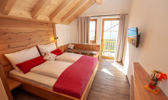 A cozy bedroom with a double bed and wooden furniture. Large windows offer a view outside and plenty of daylight.