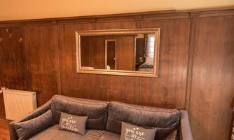 A cozy living room with a gray sofa and cushions that say "you are my sunshine." In the background, there is a large mirror and wooden paneling on the wall.