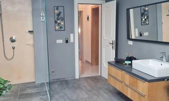 A modern bathroom with an open shower and simple, elegant furniture. The walls are in a neutral gray tone, giving the room a calm atmosphere.