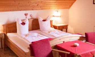 A cozy bedroom with a wooden bed frame and white bedspreads. Red chairs and a table give the room an inviting atmosphere.