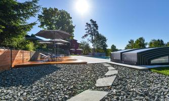 A beautiful outdoor area with a swimming pool and sun loungers. Sun umbrellas provide shade next to a modern water feature.