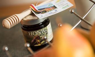 A jar of honey with a honey dipper and a card beside it. In the background, a few apples are visible.