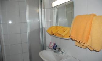 A modern bathroom with a shower, a sink, and yellow towels. The walls are tiled with white tiles.