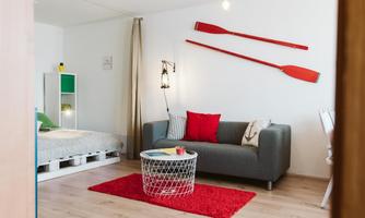 A modern living room with a gray sofa and a red pillow. Two wooden oars hang on the wall, and there is a red carpet on the floor.