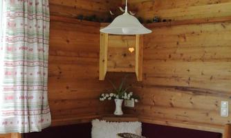 A cozy wooden dining area with a bench and a table. The walls are also made of wood, and there is a small lamp above the table.