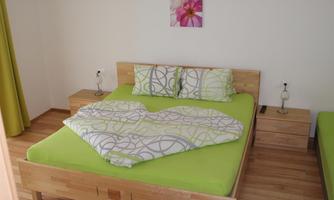 A modern bedroom with a large bed and green bedding. Bright flower pictures hang on the walls, and there is wooden furniture.