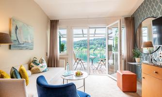 A stylish living room with modern furnishings and access to a terrace. The viewshows a peaceful landscape with water and trees.