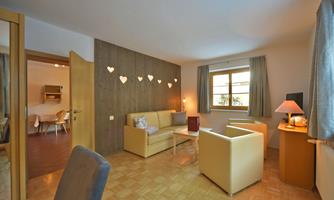 A cozy living room with a beige sofa and armchair. The room is bright and friendly, with heart decorations on the wall.