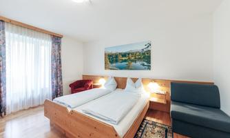 A cozy bedroom with two beds, a sofa, and a large window. A picture of a picturesque landscape hangs on the wall.