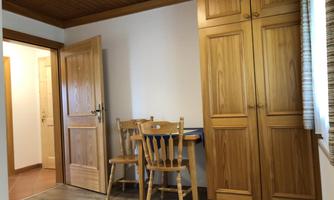 A simple room with wooden furniture. On the left side, there is a table with two chairs and a wardrobe.