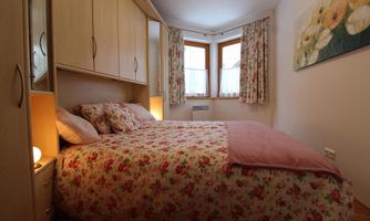 A cozy bedroom with a large bed and floral bedding. The windows are decorated with curtains, and there is soft lighting.