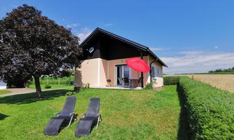A charming house with a red sun umbrella and two lounge chairs in the garden. In the background, a blue sky and green landscape can be seen.