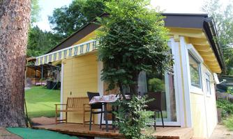 A charming yellow holiday home with a small balcony and seating. Healthy trees all around and a quiet, green environment.