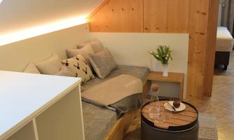 A cozy living room with seating and wooden paneling. On the table is a vase with fresh flowers and some snacks.