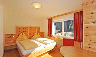 A cozy bedroom with a large window and wooden decor. The beds are neatly made and a round table is in the room.
