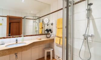 A modern bathroom with a shower and large mirrors. The walls are tiled in light colors, and yellow towels provide a colorful accent.