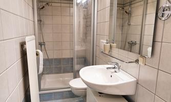 A modern bathroom with a shower, sink, and mirror. The walls are tiled and there are towels on a white stool.