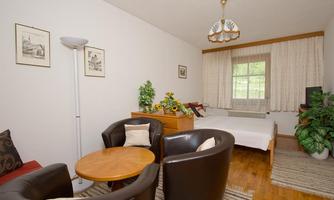 A cozy room with a table and two armchairs. The room has windows with curtains and is decorated with plants.