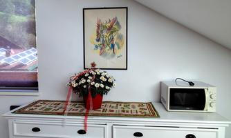 A cozy room with a white sideboard and a microwave. On the sideboard, there is a bouquet of flowers and a colorful piece of art on the wall.
