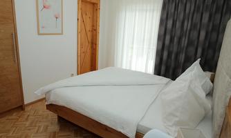 A stylish bedroom with a wooden bed and white bedspreads. The room has large windows that let in daylight and a peaceful atmosphere.