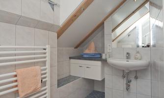 A modern bathroom with slanted walls and a window in the roof. The walls are brightly tiled and there is a sink unit as well as a towel holder.