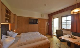 A cozy room with a double bed and wooden furniture. There is a table with chairs and a view outside.
