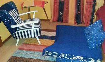 A cozy room with a blue armchair and a blue chaise lounge. The floor is covered with a colorful carpet, and the walls are decorated in warm colors.