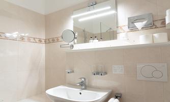 A modern bathroom with a sink and a large mirror. The walls are in light colors and there are toiletries on the shelf.