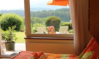 A cozy bedroom with a view of a green garden and a tranquil landscape. Outside, there are comfortable chairs and a parasol.