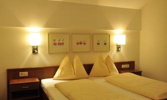 A cozy bedroom with a large double bed and two pillows. Pictures hang on the wall, and there is soft lighting.