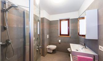 A modern bathroom with a glass shower and a white sink. The walls are painted in neutral shades of gray.