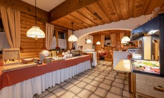 A cozy restaurant with wood paneling and warm lighting. A long buffet counter with various dishes is in the foreground.
