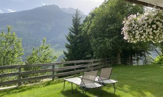 A peaceful garden with two loungers and a beautiful view of the mountains. In the background, trees and flowers are visible.