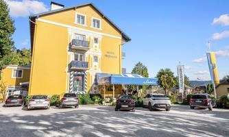 A charming yellow hotel with an inviting entrance area. In the foreground, several cars are parked on a gravel parking lot.