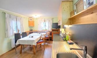 A bright kitchen with a dining table and chairs. The walls are painted in soft colors and there are wooden shelves.