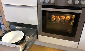 A modern kitchen with an oven where fresh rolls are being baked. Additionally, a pot is visible in a drawer.