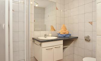 A modern bathroom with a shower, a sink, and a toilet. The walls are tiled and there is a beige carpet on the floor.