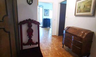 A narrow hallway with wooden flooring and a red chair. Pictures hang on the wall, and two wall sconces provide pleasant lighting.