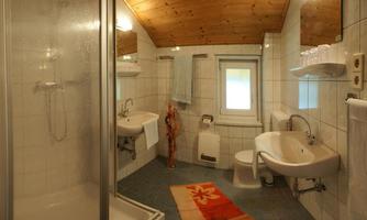 A modern bathroom with a shower, sink, and toilet. The walls are tiled and the ceiling has wooden beams.
