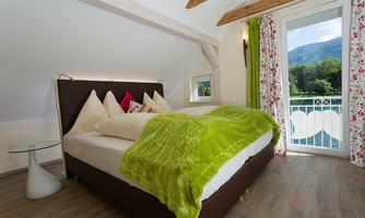 A cozy bedroom with a large bed and a green blanket. The window offers a view of the surrounding nature.