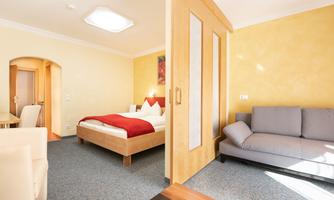 A bright room with a double bed and a cozy sofa. The walls are painted in warm colors and the room feels inviting.