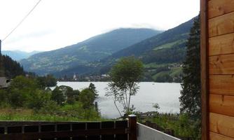 A view of a lake surrounded by mountains and trees. The sky is cloudy and there is a relaxed atmosphere.
