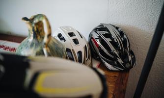 Three bicycle helmets are lying on a table, next to a decorative kettle. The helmets are in different colors and designs.