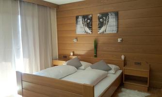 A modern bedroom with a wooden bed and two pillows. The walls are in a warm wood tone, and there are large curtains as well as decorative pictures.