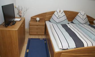 A cozy bedroom with a large bed and striped bedcovers. There is also a television and a wooden piece of furniture on the other side of the room.