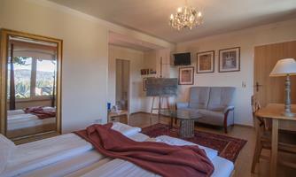 A cozy room with two beds, a large mirror, and a comfortable armchair. Various pictures hang on the wall, and the light is friendly and inviting.