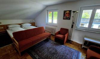 A cozy bedroom with a double bed and a red sofa. Large windows let in plenty of daylight and offer a view of the outside.