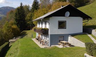 An idyllic house in nature, surrounded by green meadows and trees. In the background, gentle hills can be seen.